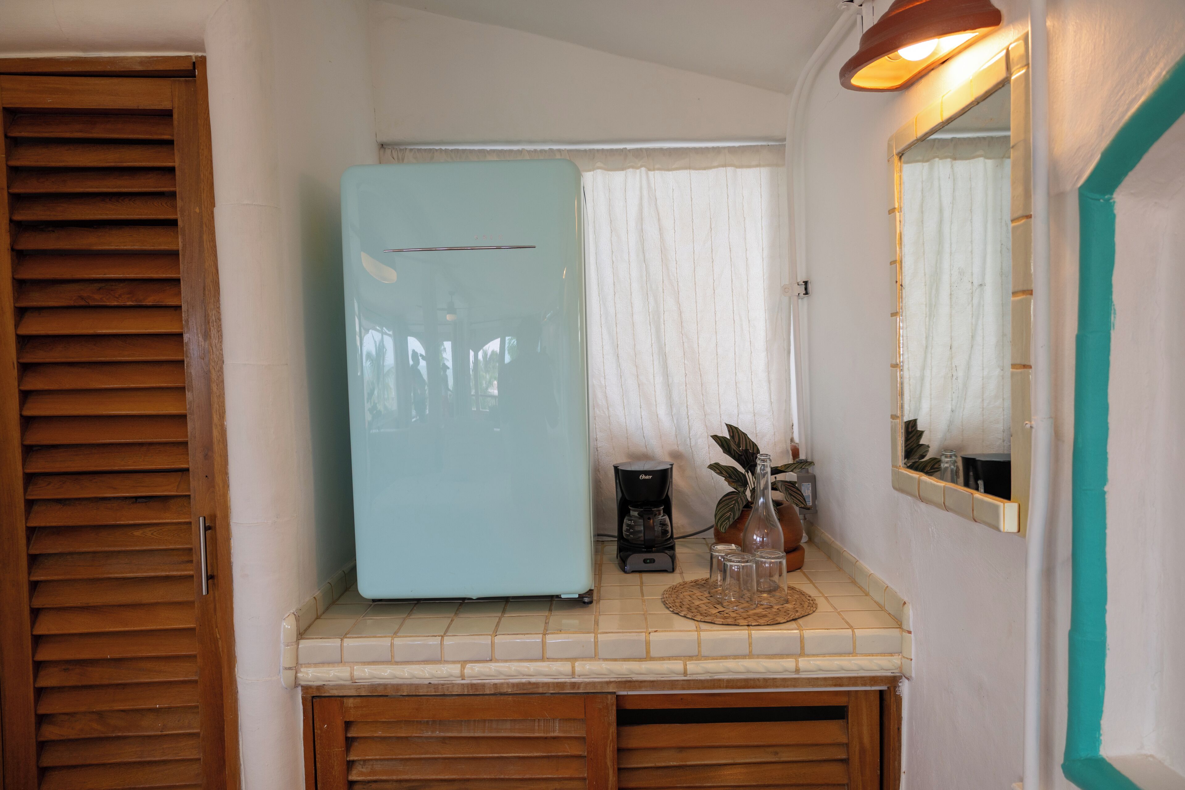 A compact kitchen with a light blue refrigerator, a coffee maker, and a potted plant on the counter.