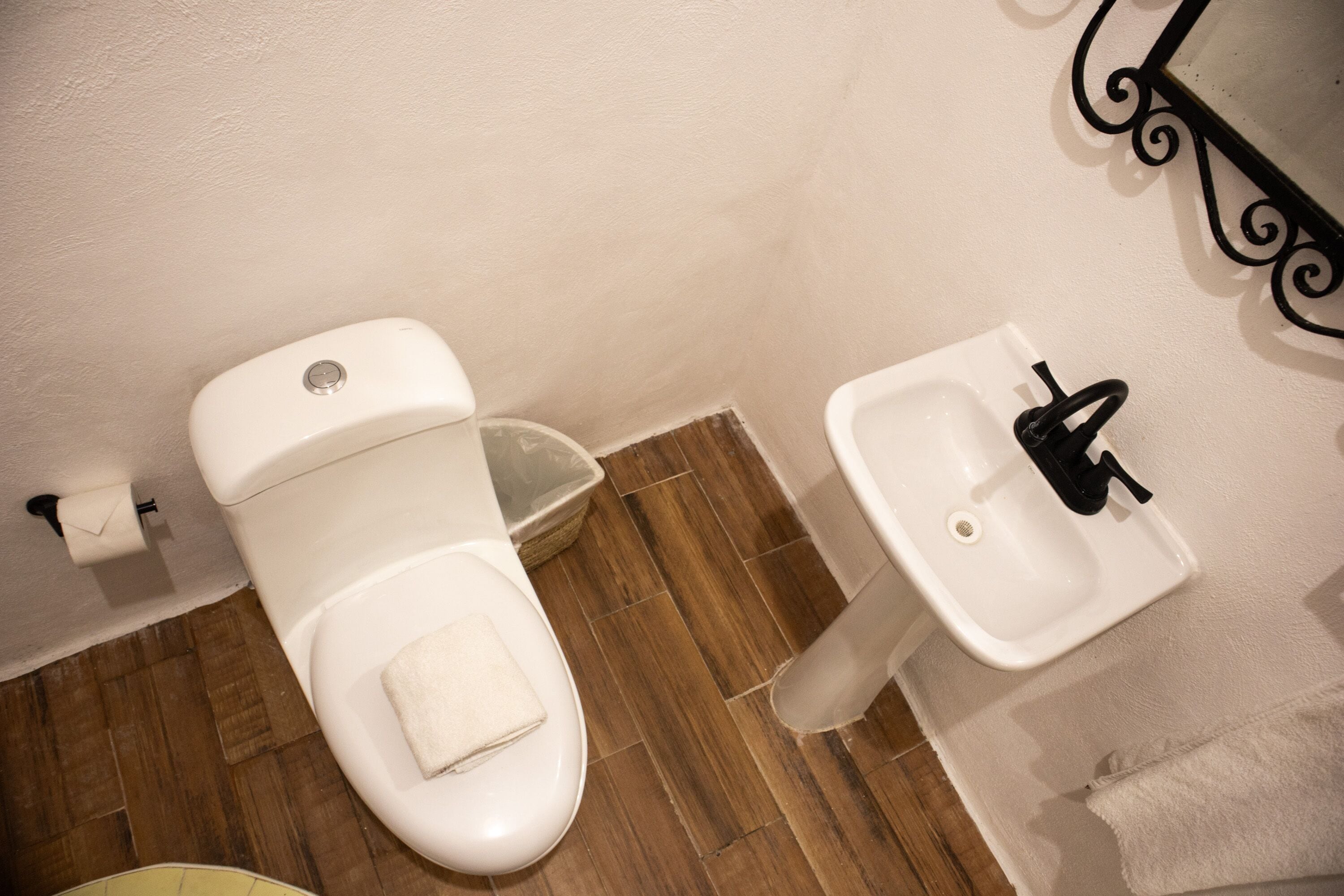 Baño con inodoro, lavamanos y suelo de madera.