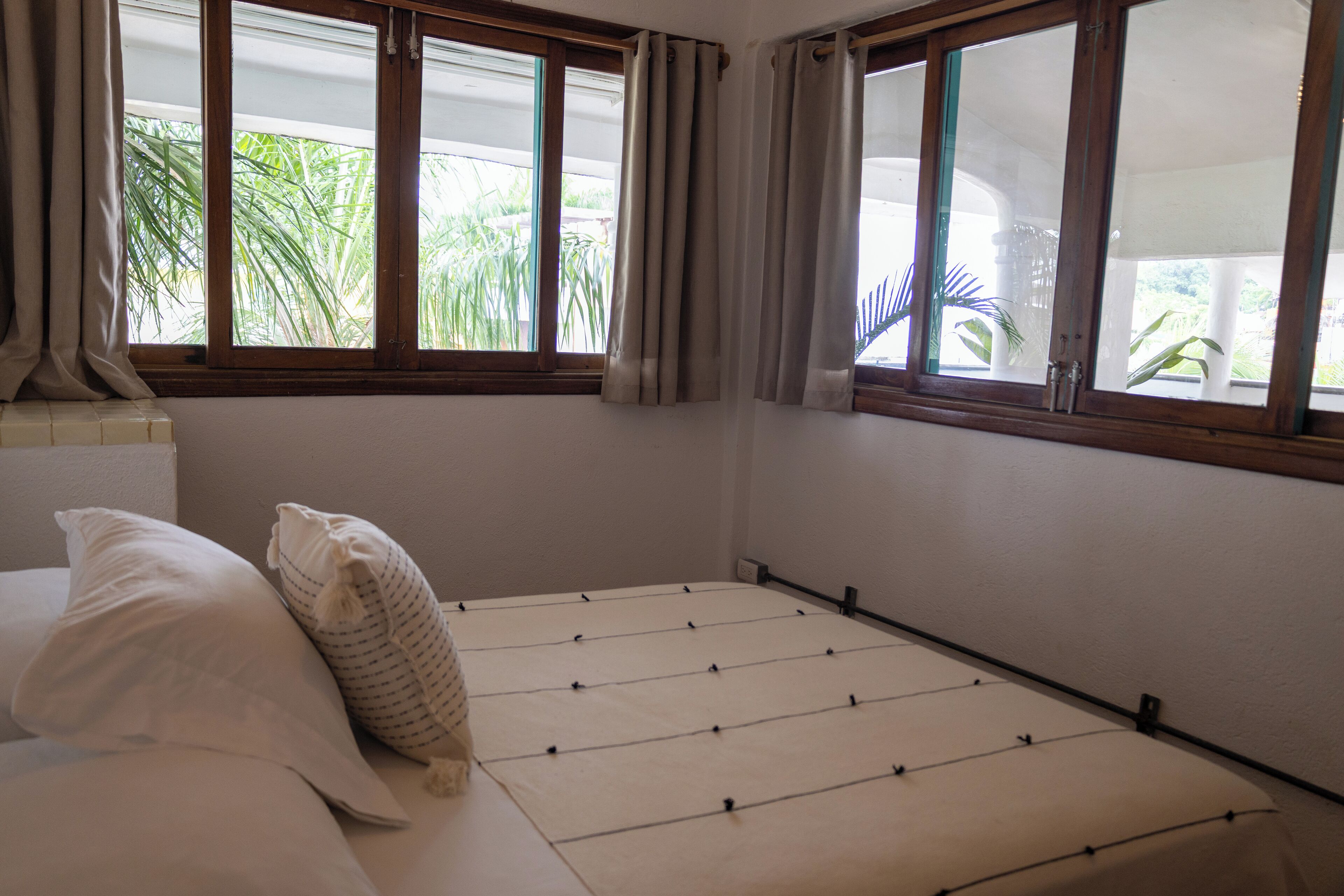 A room with a bed, a window with curtains, and a view of palm trees outside.