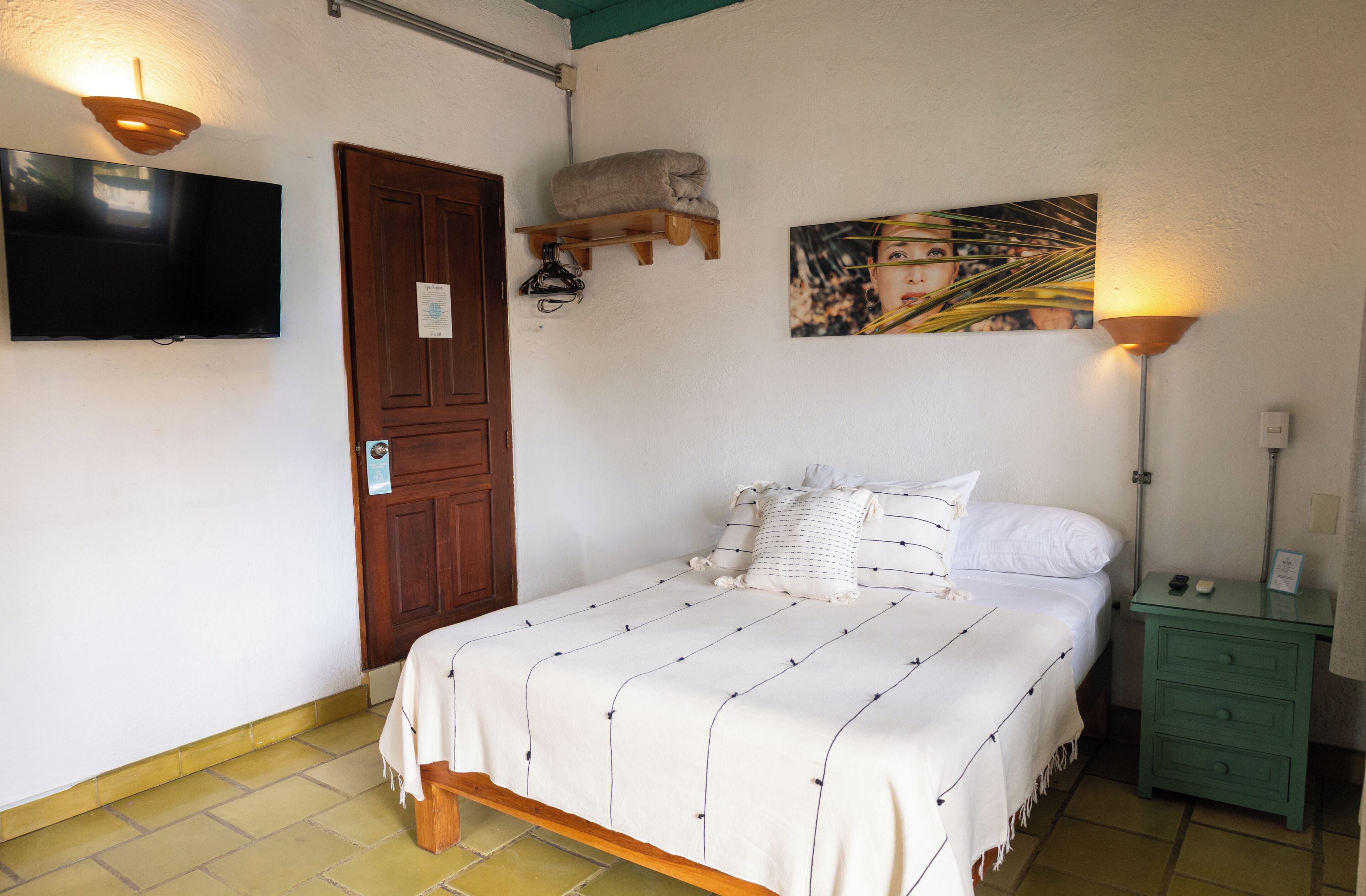 A neatly arranged bedroom with a bed, a television, a painting, and a nightstand.