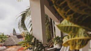 A hammock on a balcony with potted plants and a thatched-roof structure in the background. - Sayulita Central Hotel (Sayulita)