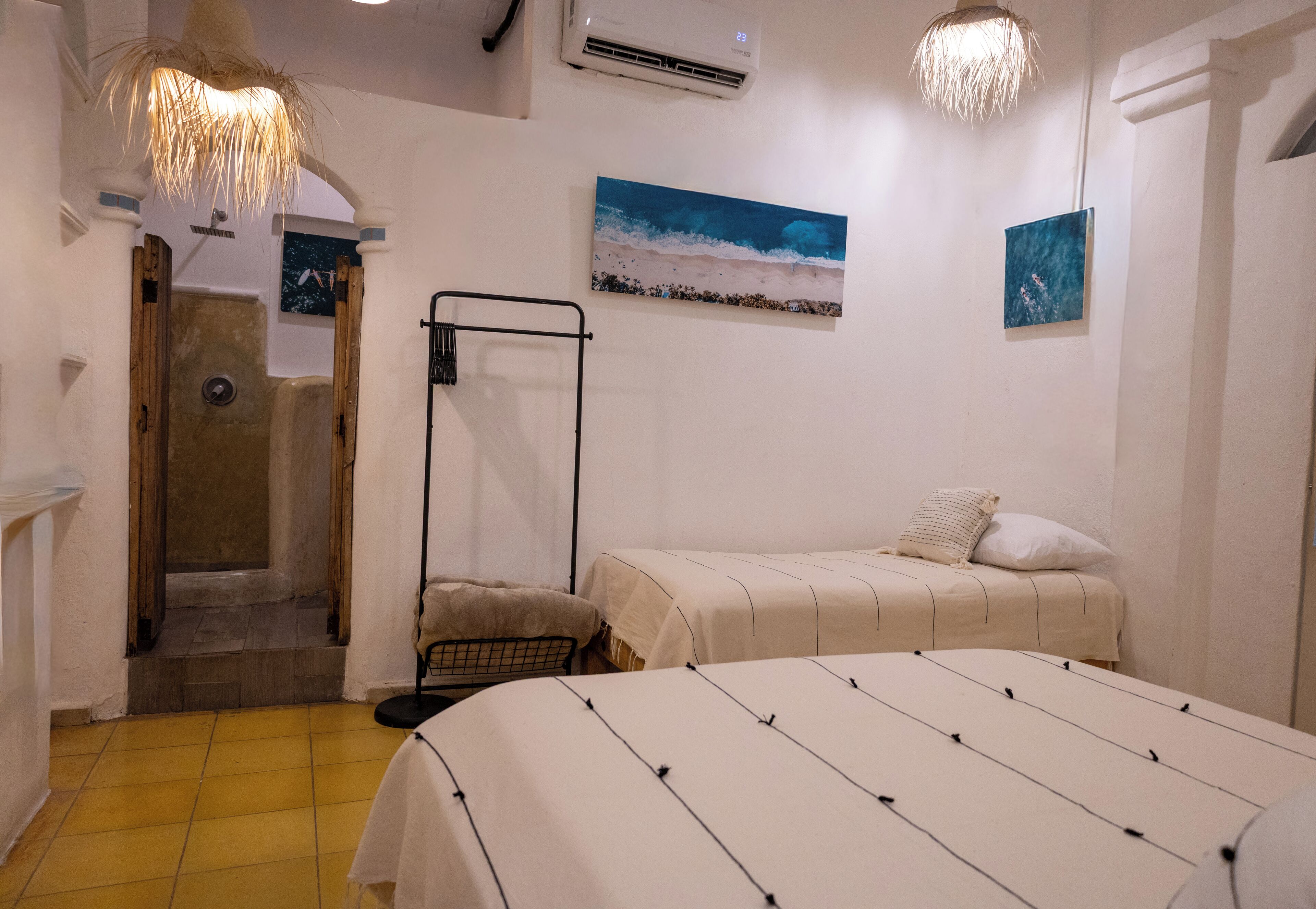 A bedroom with a bed, a nightstand, a wall-mounted shelf, a towel rack, and a shower area.
