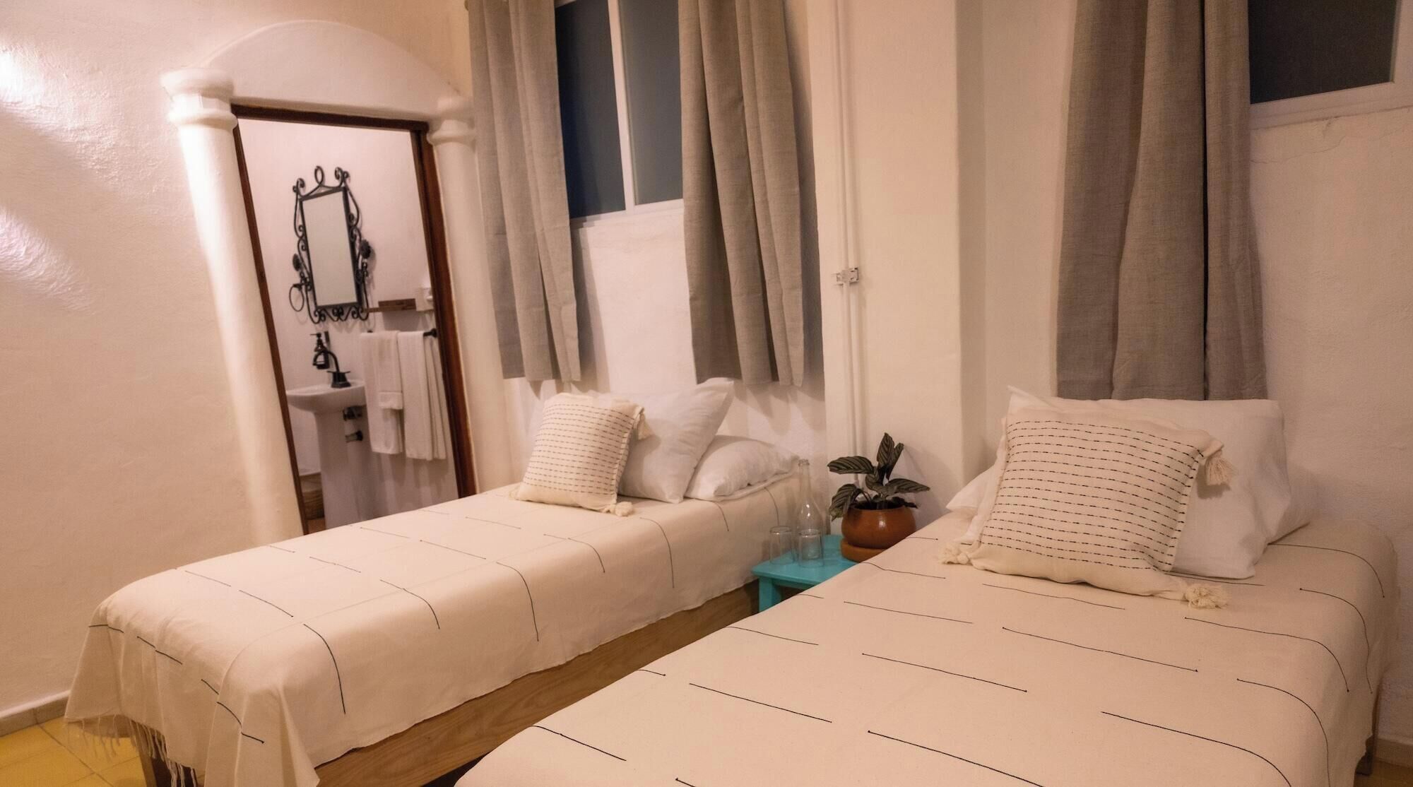 A bedroom with two beds, a small table, a potted plant, and a bathroom visible through an archway.