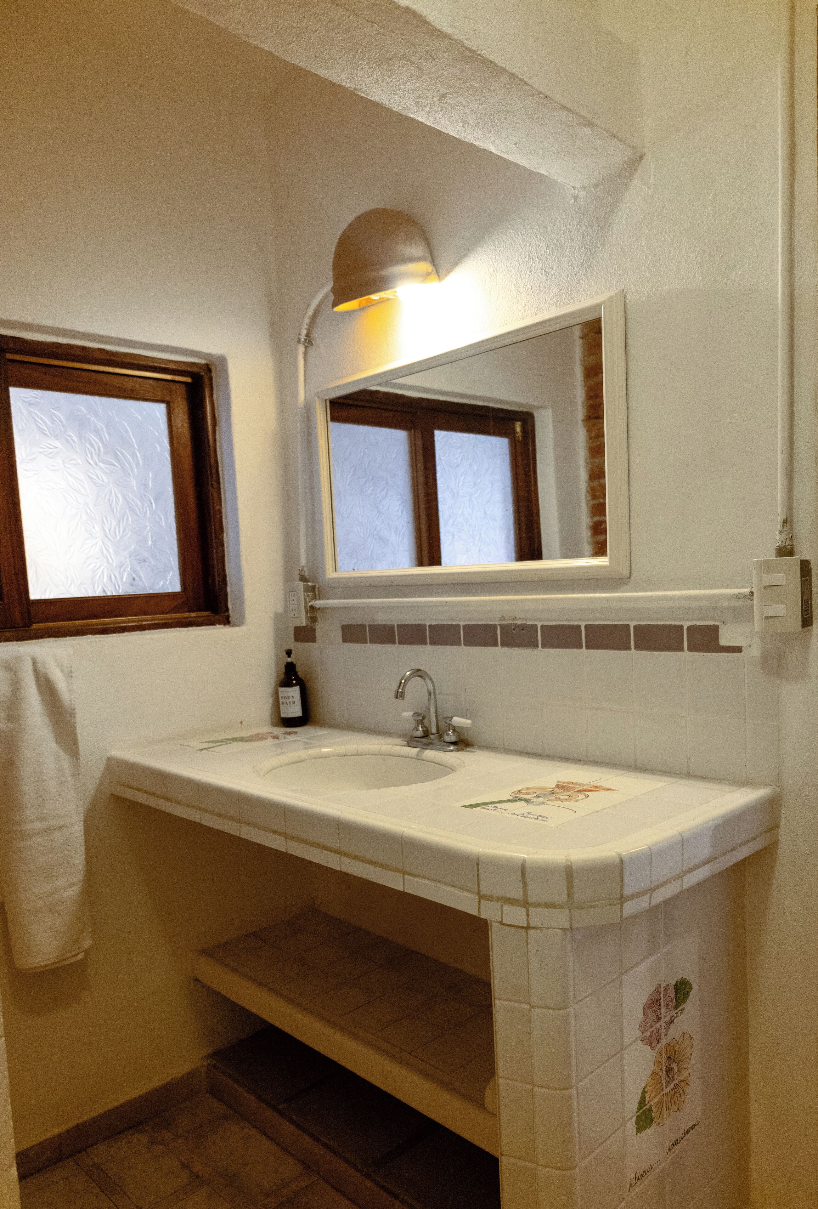Un baño con un lavamanos blanco, un espejo encima y una ventana con marco de madera.