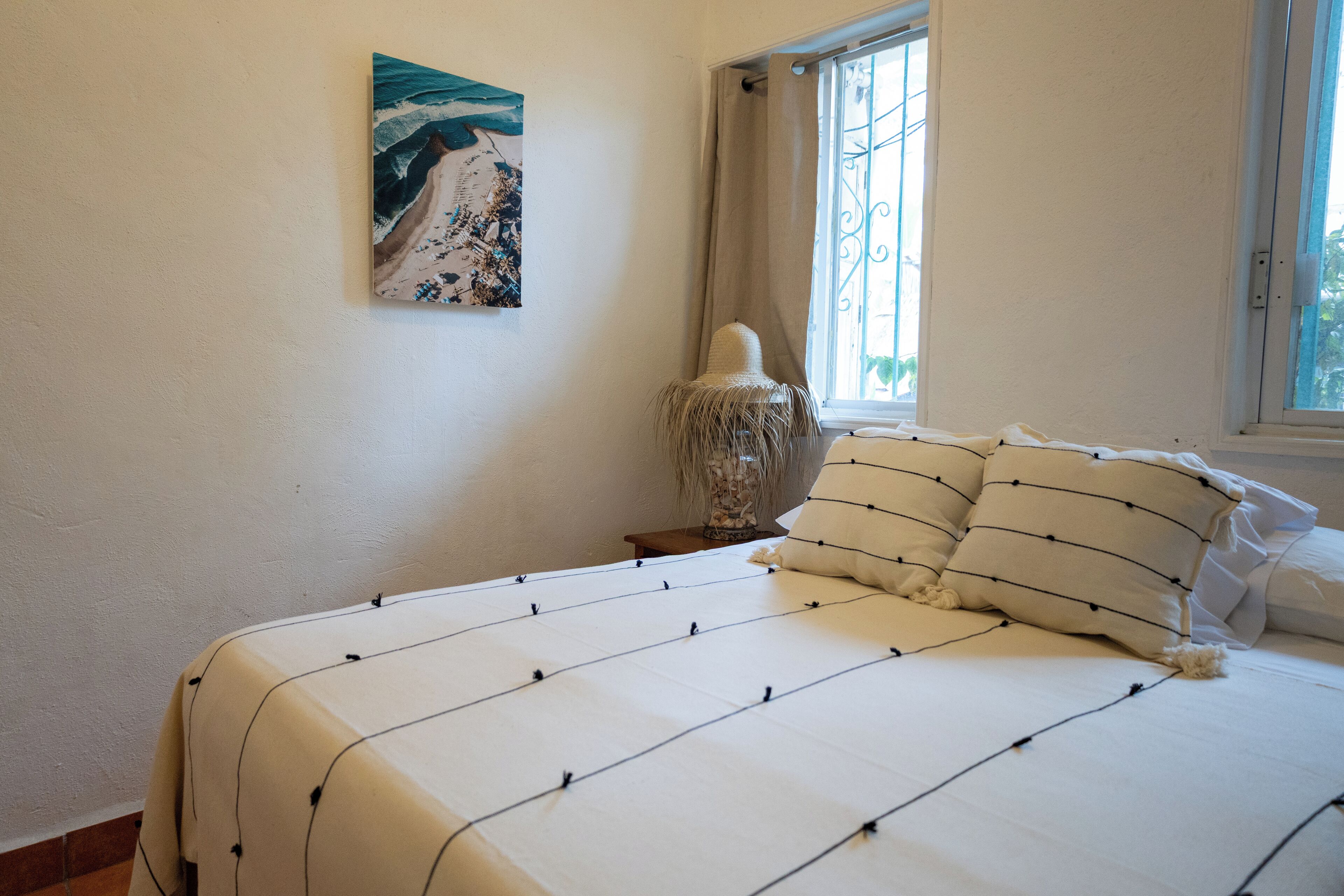 Una cama bien hecha con un cojín a rayas y un jarrón decorativo sobre una mesita de noche.