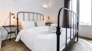 Ein ordentlich bezogenes Bett mit weißen Leinentüchern, einem schwarzen Metall-Kopfstück und zwei Nachttischen mit Lampen.
