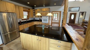 A spacious kitchen with wooden cabinets, a stainless steel refrigerator, a large island with a stove, and a ceiling fan.