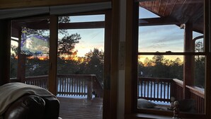 A room with a large window overlooking a deck and a sunset view.