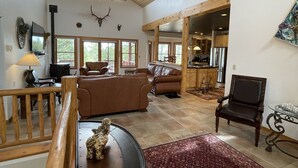 A spacious living room with a high ceiling, wooden beams, a fireplace, and a large window.