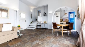 Un salón espacioso con sofá, mesa de comedor y sillas, una escalera que conduce a otra habitación y una puerta azul.