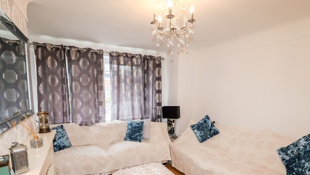 A bedroom with two beds, a chandelier, a bedside table with a lamp, and a window with patterned curtains. - The Hawthorns (Chester)