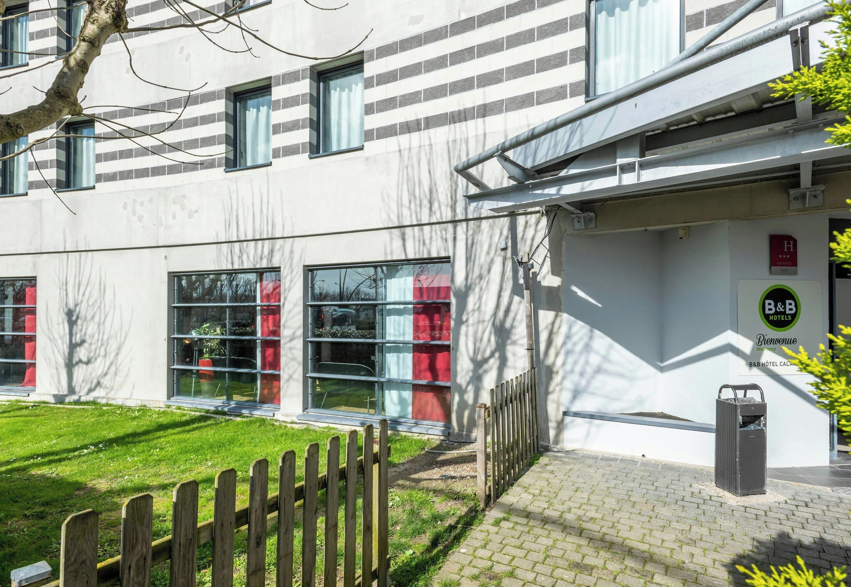 L’extérieur d’un hôtel au design moderne, avec une façade en briques, de grandes fenêtres et une entrée fermée par un portail.