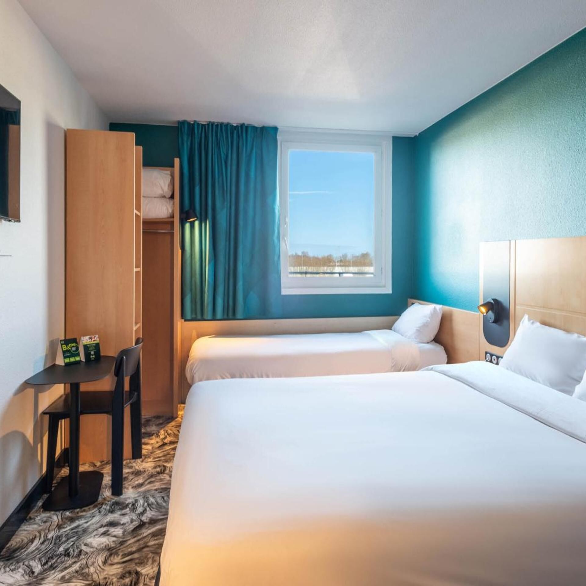Een hotelkamer met twee bedden, een bureau, een stoel, een kledingkast en een raam met uitzicht.