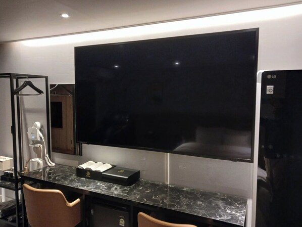 Una habitación de hotel moderna con un televisor de pantalla plana grande montado en la pared, una encimera de mármol y un minibar.