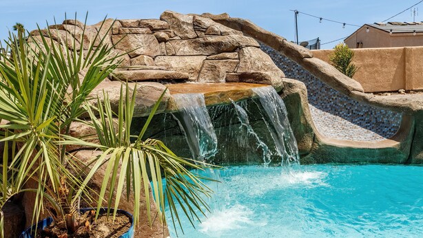 Ein Pool mit Wasserfall, umgeben von Felsen und einer Palme.