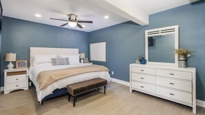 Ein Schlafzimmer mit Bett, Nachttischen, Kommode, einer Bank, einem Deckenventilator und einem großen Spiegel.