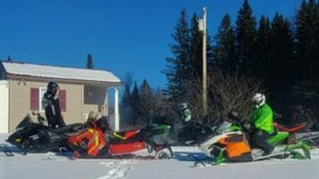 A group of snowmobiles parked in a snowy area with a small building in the background.