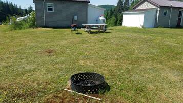 A grassy yard with a metal grill and a picnic table.