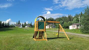 A playground with a swing set and climbing structure in a grassy field with houses in the background.