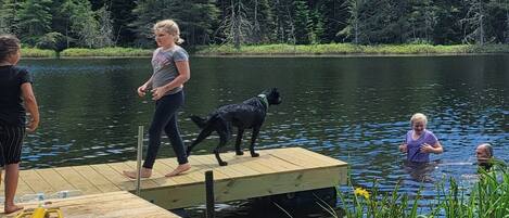 Eine Holzstege, der sich in einen See erstreckt, mit Menschen und einem Hund darauf.