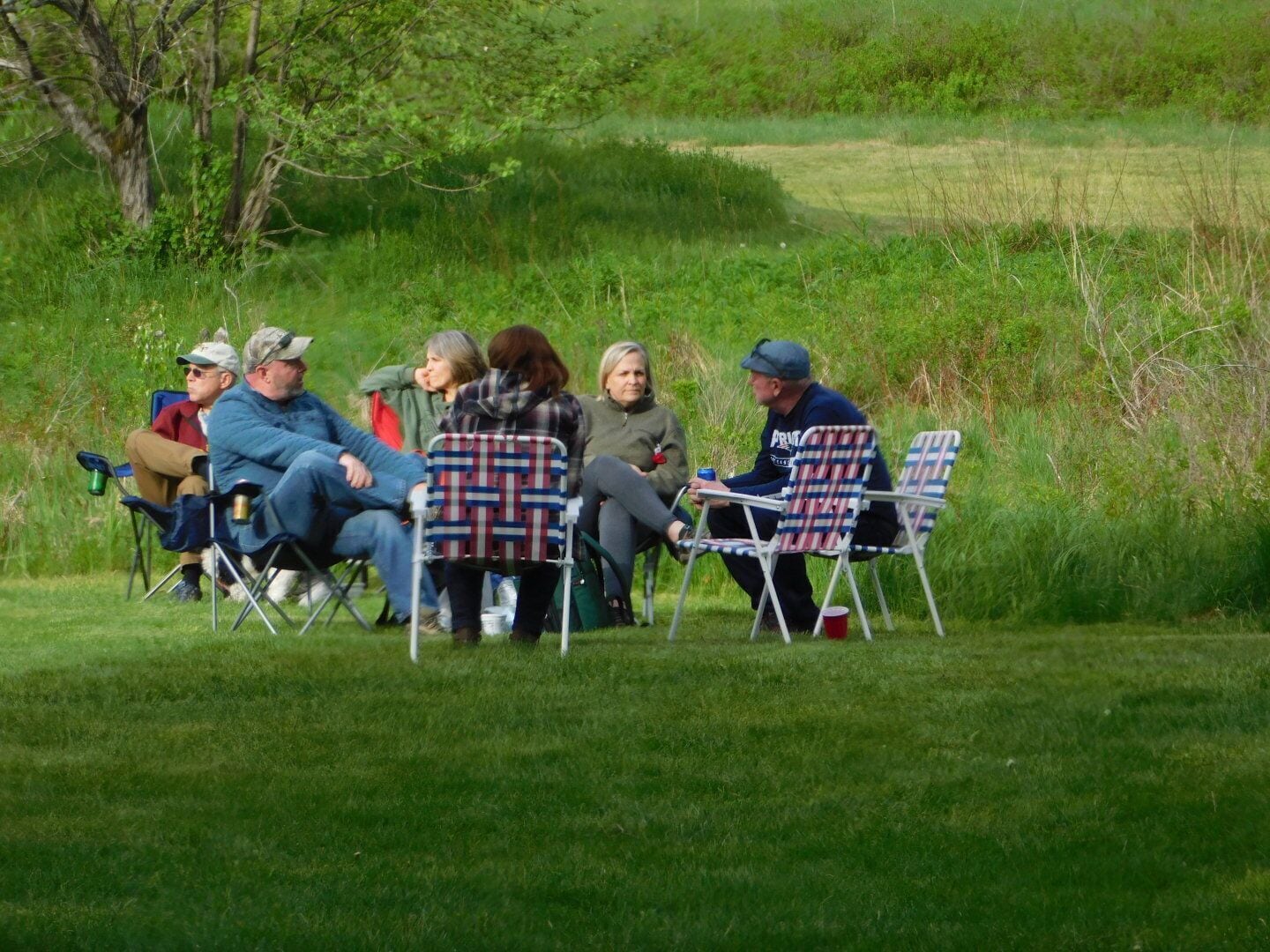 Un groupe de personnes assises sur des chaises de jardin dans un espace extérieur verdoyant.