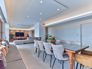 A modern living room with a stone accent wall, a large flat-screen TV, and a dining area with a glass-top table and cushioned chairs.