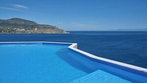 Una piscina infinita de color azul intenso con vista al mar y una montaña distante.