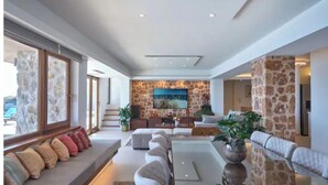 Amplia sala de estar con una pared de acento de piedra, un televisor de pantalla plana grande y una zona de estar cómoda con cojines.