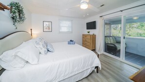 A bedroom with a bed, a dresser, a TV, and a balcony with outdoor furniture.