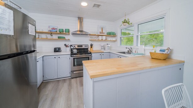 A modern kitchen with stainless steel appliances, wooden countertops, and white cabinetry.