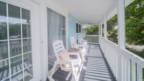 A covered porch with white chairs and a table, overlooking a green landscape.