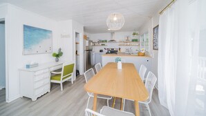 A modern kitchen with white cabinets, a wooden dining table, and a hanging light fixture.