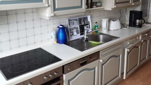 A kitchen with white cabinets, a black stove, a sink, and a coffee maker. - FeWo - Feeling at home (Wilhelmshaven)