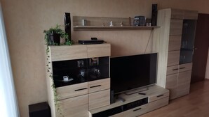 A modern living room with a large flat-screen TV, wooden cabinets, a coffee table, and a small plant. - FeWo - Feeling at home (Wilhelmshaven)