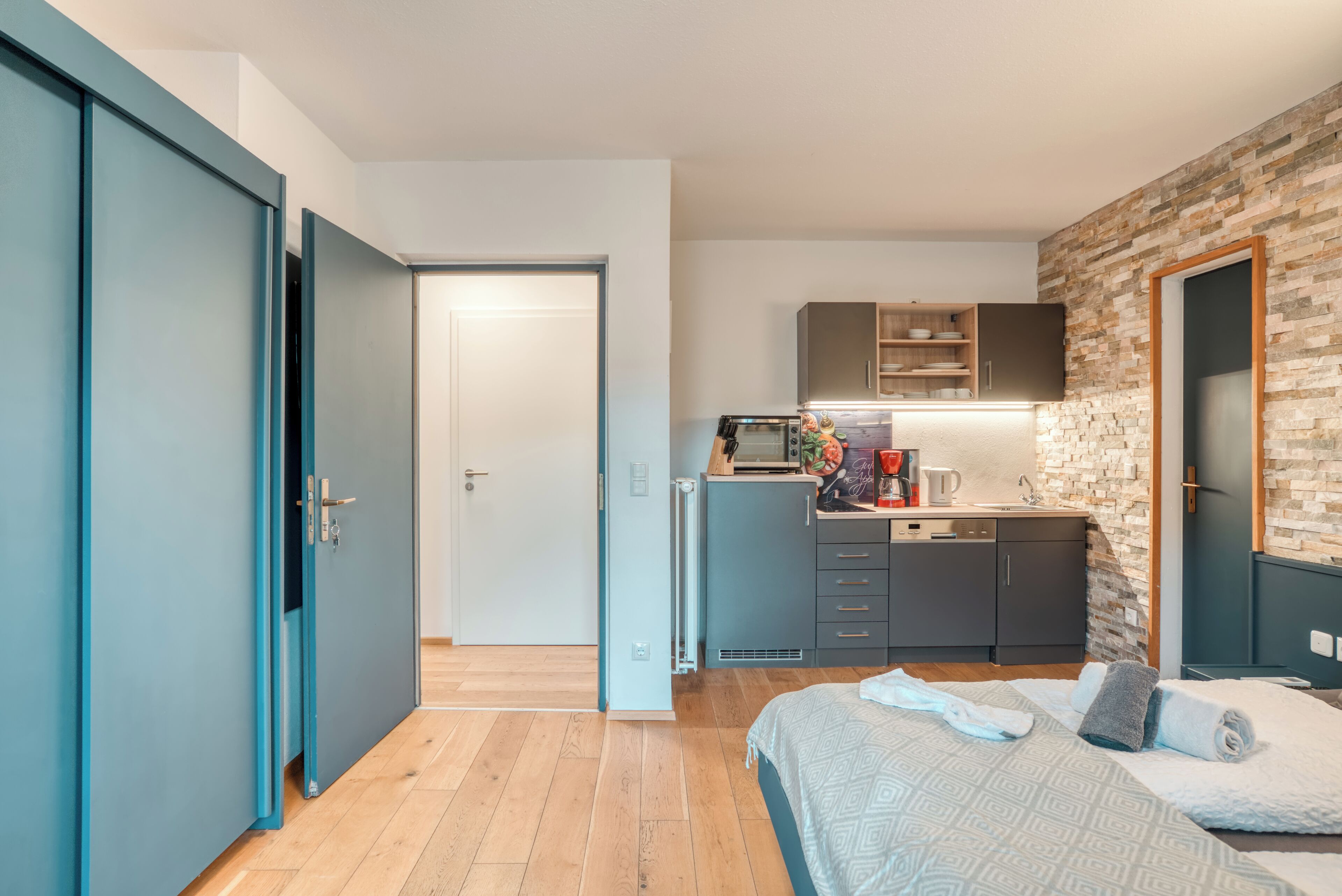 A modern bedroom with a bed, a wardrobe, and a kitchenette.