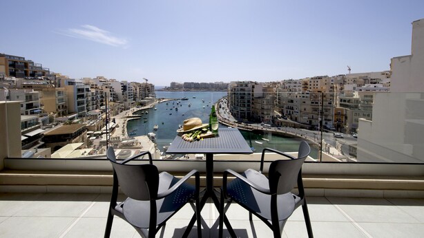 A balcony with two chairs and a table, overlooking a marina with boats and buildings.