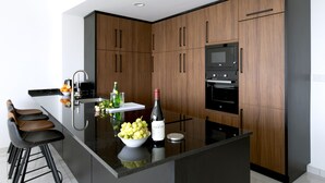 A modern kitchen with dark wood cabinets, a central island with a bowl of fruit, a wine bottle, and bar stools.