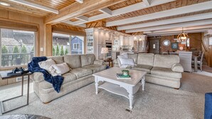 A spacious living room with a large sectional sofa, a coffee table, and a view of the backyard through large windows. - Private Beachfront Home w/ Hot Tub - Walk to Restaurants, Coffee and More! (Allyn)