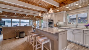 A spacious kitchen with a large island, wooden ceiling beams, and a view of the outdoors. - Private Beachfront Home w/ Hot Tub - Walk to Restaurants, Coffee and More! (Allyn)