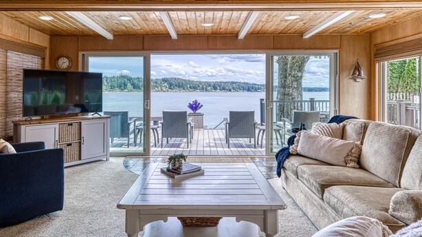 A wooden interior with a TV, sofa, and a view of a lake. - Private Beachfront Home w/ Hot Tub - Walk to Restaurants, Coffee and More! (Allyn)