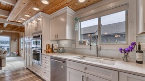 A modern kitchen with white cabinets, stainless steel appliances, and a large window with a view of the outside. - Private Beachfront Home w/ Hot Tub - Walk to Restaurants, Coffee and More! (Allyn)