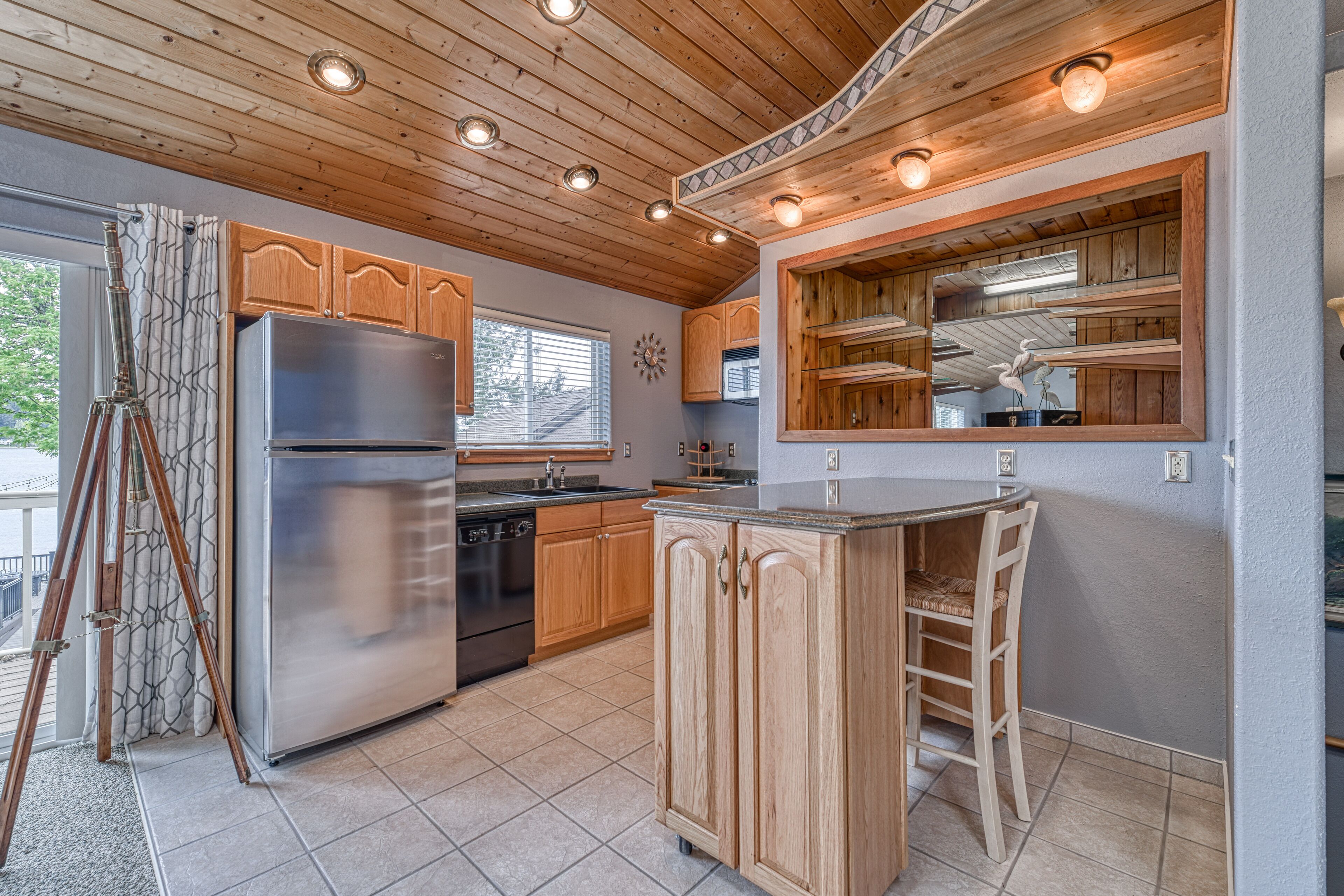A modern kitchen with wooden cabinets, a stainless steel refrigerator, and a large island with bar seating.