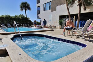 Relax by the pool with a hot tub and lounge chairs, surrounded by palm trees.