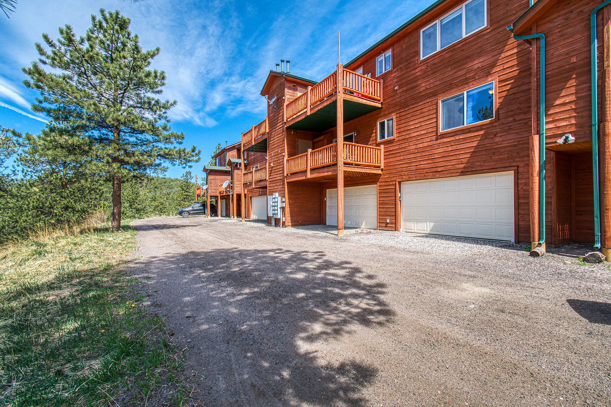 A two-story wooden cabin with a gravel driveway, a covered front porch, and a garage.