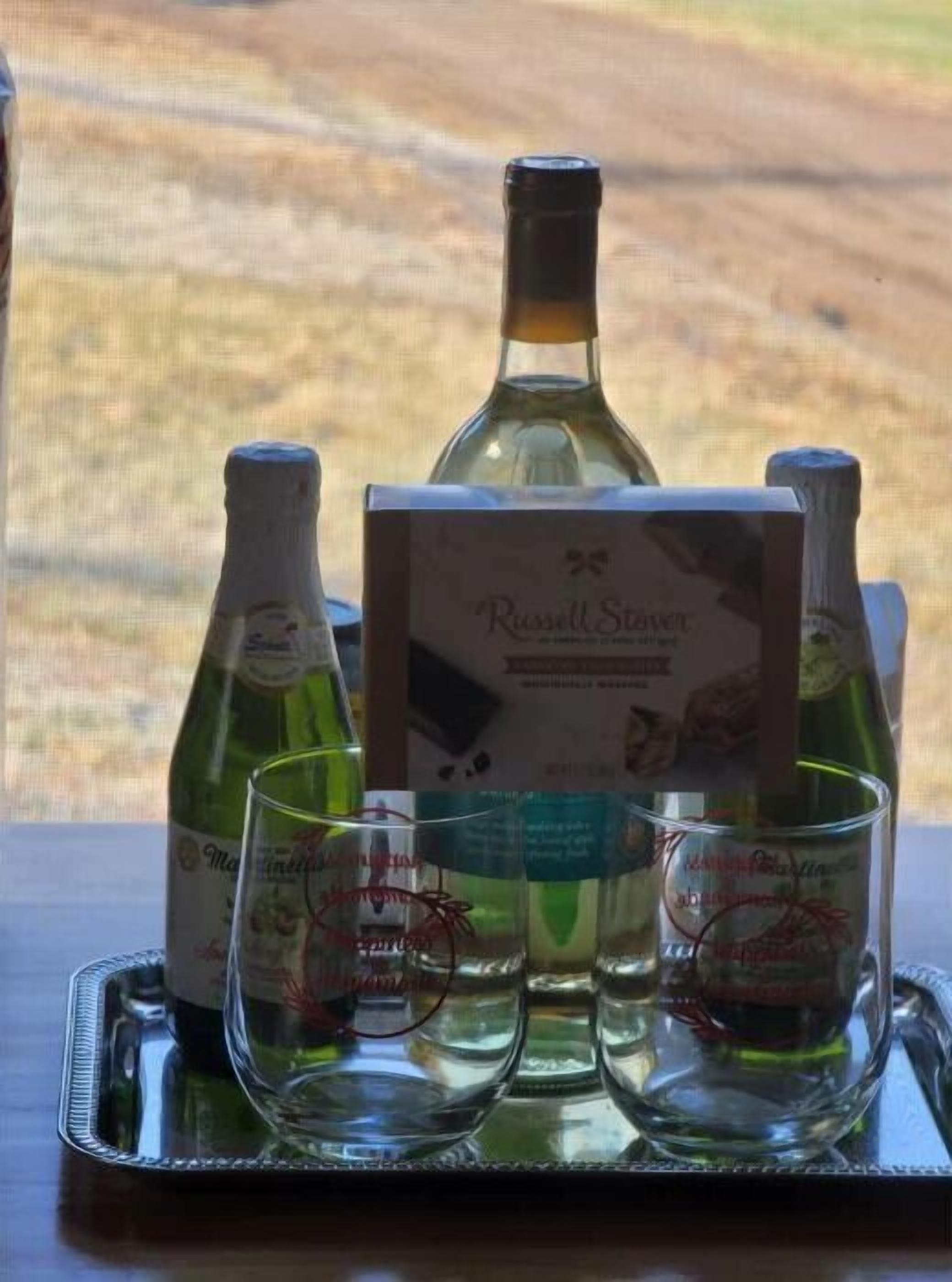 Un plateau avec des bouteilles de vin et des verres, posé sur une table offrant une vue sur un paysage naturel.