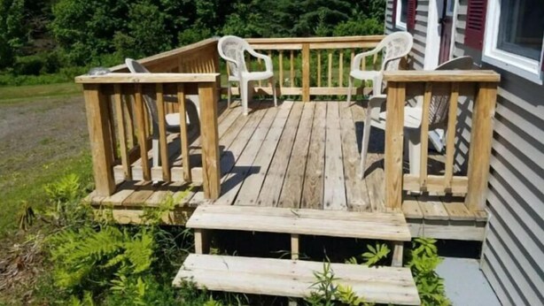 A wooden deck with two white plastic chairs and a small table. - 01) The Bear Cave Cabin (Stewartstown)