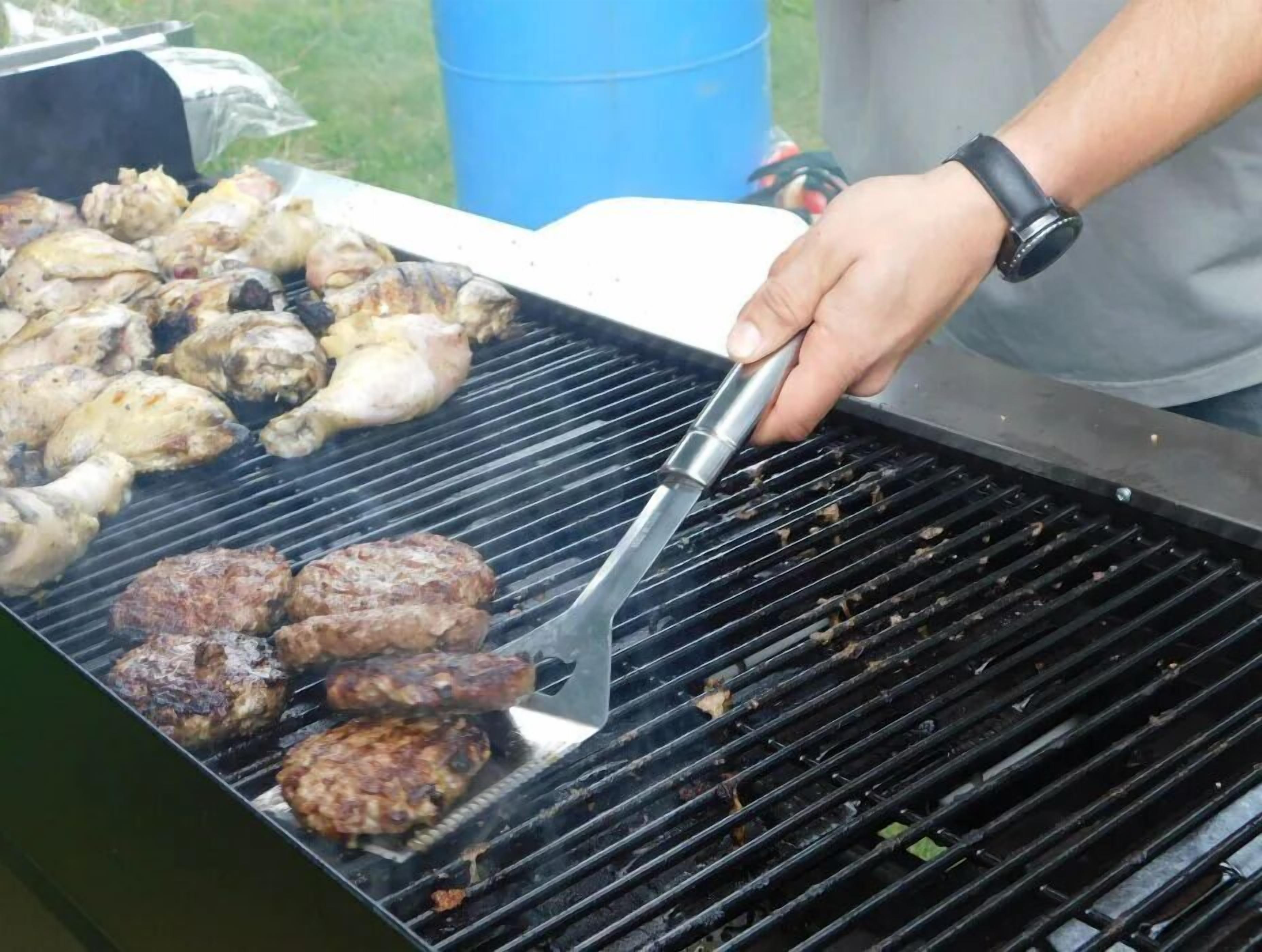 Une personne qui fait griller du poulet et des hamburgers sur un barbecue extérieur.