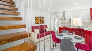 En modern inredning med en trätrappa, en röd soffa, ett matbord för fyra personer och ett köksområde med röda skåp.