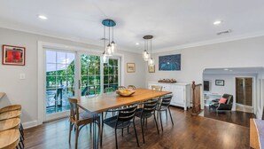 A spacious dining area with a wooden table and chairs, large windows, and pendant lighting.