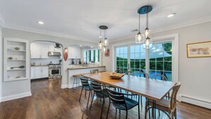 A modern kitchen with white cabinets, a stainless steel oven, and a wooden dining table with chairs.